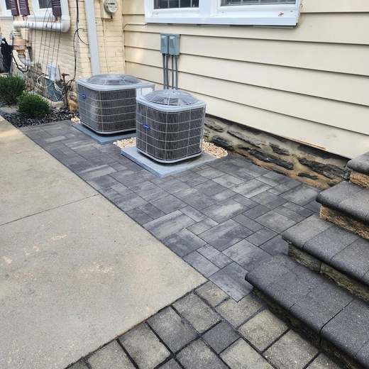 After: the same condensers standing on a level paver pad with a soldier-course border, tied into the concrete walk and the stone steps.