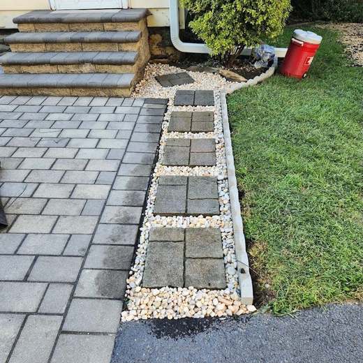 After: the same stepping pavers reset level in white river stone with a clean curb edge along the lawn.